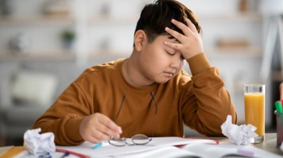 A child cradling his head in his hands, frustratedly leaning over his homework. Difficulty learning nursery rhymes could be a sign of dyslexia