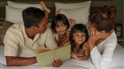 Parents reading with their two daughters in bed
