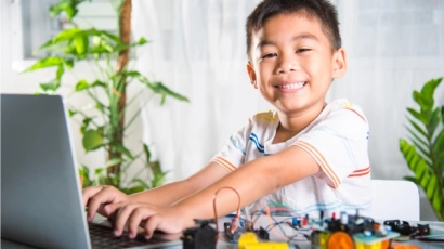 Asian boy at the computer surrounded with robotic parts, illustrating that improving physical quotient improves cognitive development