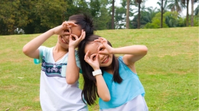 Children smiling in front of a lawn, with their hands cupped over their eyes