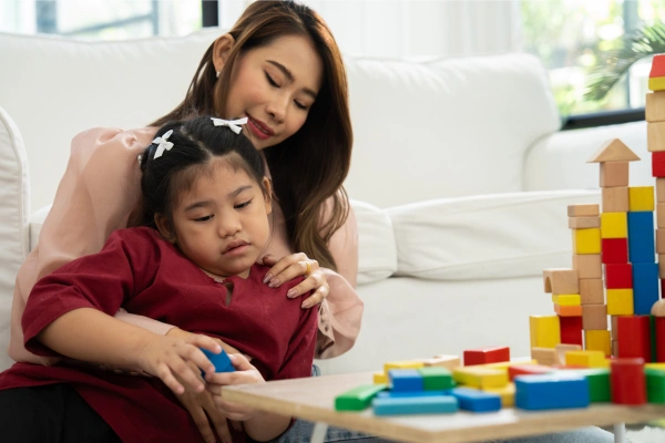 Child in special education needs curriculum playing with blocks, being held by her teacher