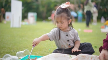 Little girl playing with tubs of paint on a field. Children with special needs may prefer to play alone, which could be a challenge in terms of social interaction
