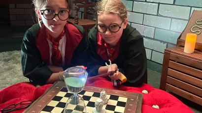 Image of children dressed in wizarding robes in front of a chessbaord, at the Chamber of Secrets escape room for kids at The Tiara Society