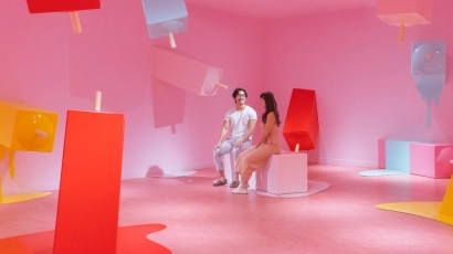 A couple seated on a bench shaped like a giant potong ice cream, surrounded by similar giant potong ice cream sculptures in a pink room in the Museum of Ice Cream