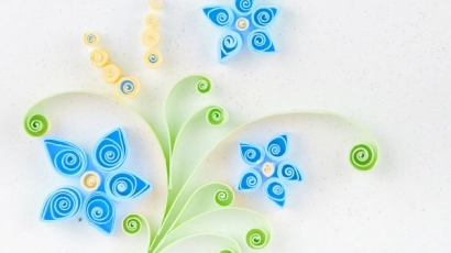 Paper quilling art of three blue flowers from green stems, with two yellow buds