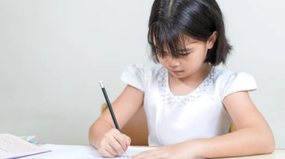 Asian girl writing on a desk. AEPS is a standardised assessment to evaluate the developmental level of children with disabilities.