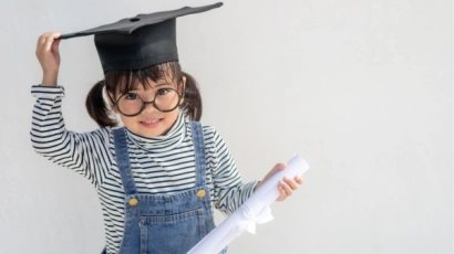 Asian girl with pigtails wearing a graduation cap, and holding a scroll in her hands. She is dressed in a striped black and white long sleeved shirt with a denim overall.