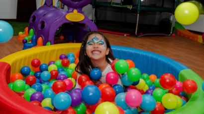 Little girl with her face painted, grinning from a ball pit. The PA Family PLAYGround, one of the family fun deals listed here, includes a similar ball pit.