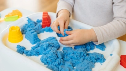 Hands kneading blue kinetic sand, which is an excellent form of sensory play for toddlers.
